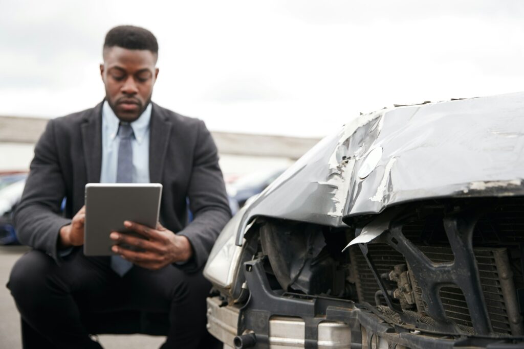 Male Insurance Loss Adjuster With Digital Tablet Inspecting Damage To Car From Motor Accident